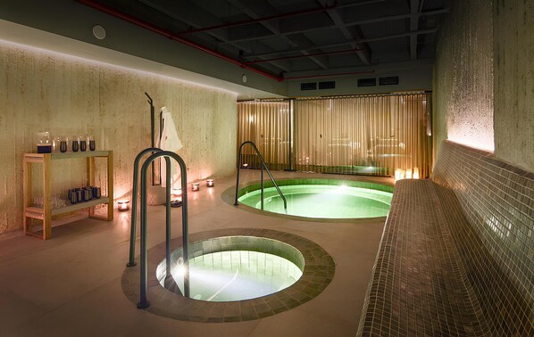 A spa area with two hot tubs, a wooden shelf with bottles, and a bench. - Wellcomm Spa & Hotel (Medellín)