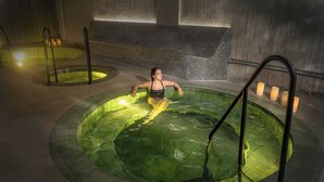 A person in a green, leaf-patterned hot tub with a tiled wall and a bench in the background. - Wellcomm Spa & Hotel (Medellín)