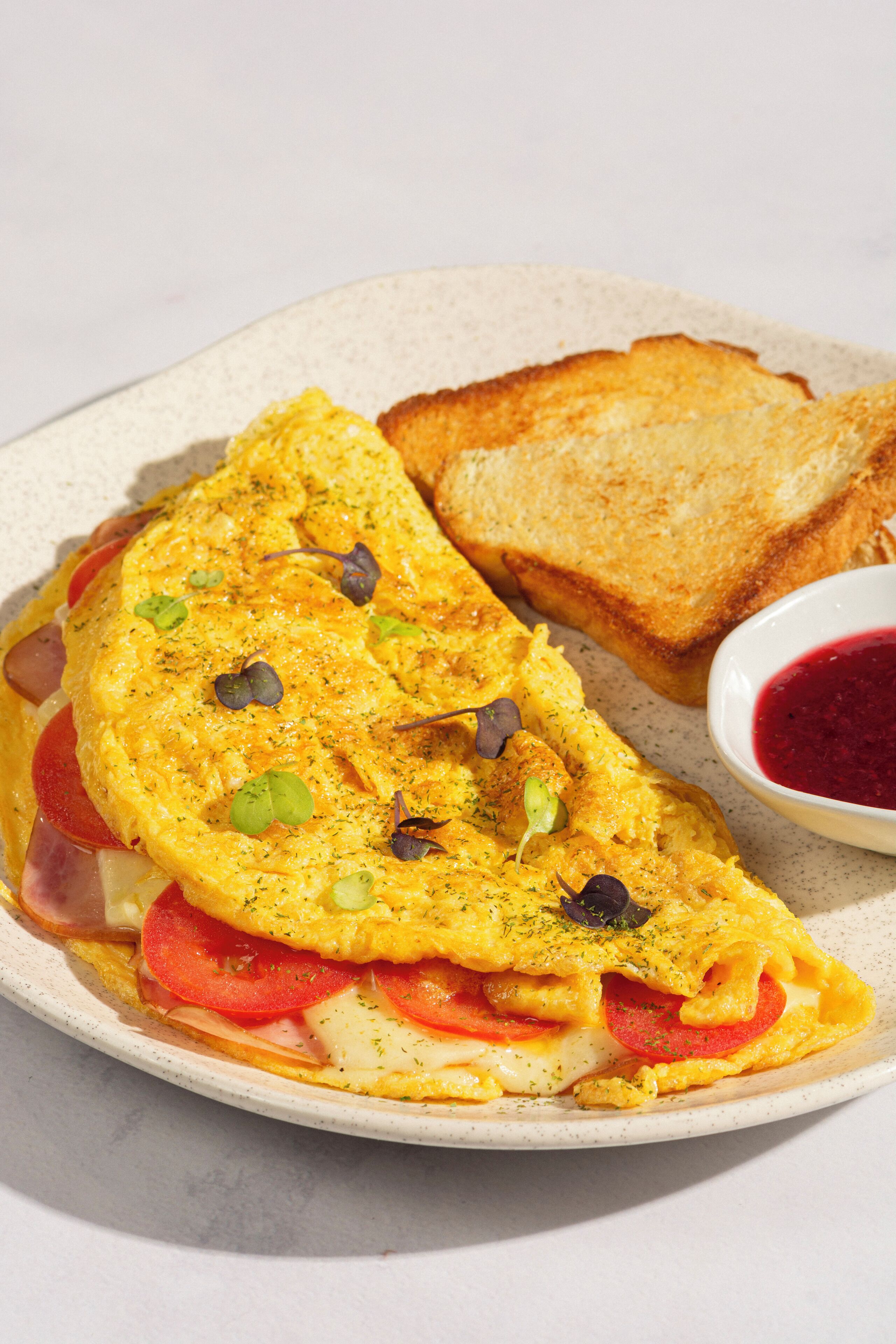 A plate with an omelette, toast, and a small bowl of jam.