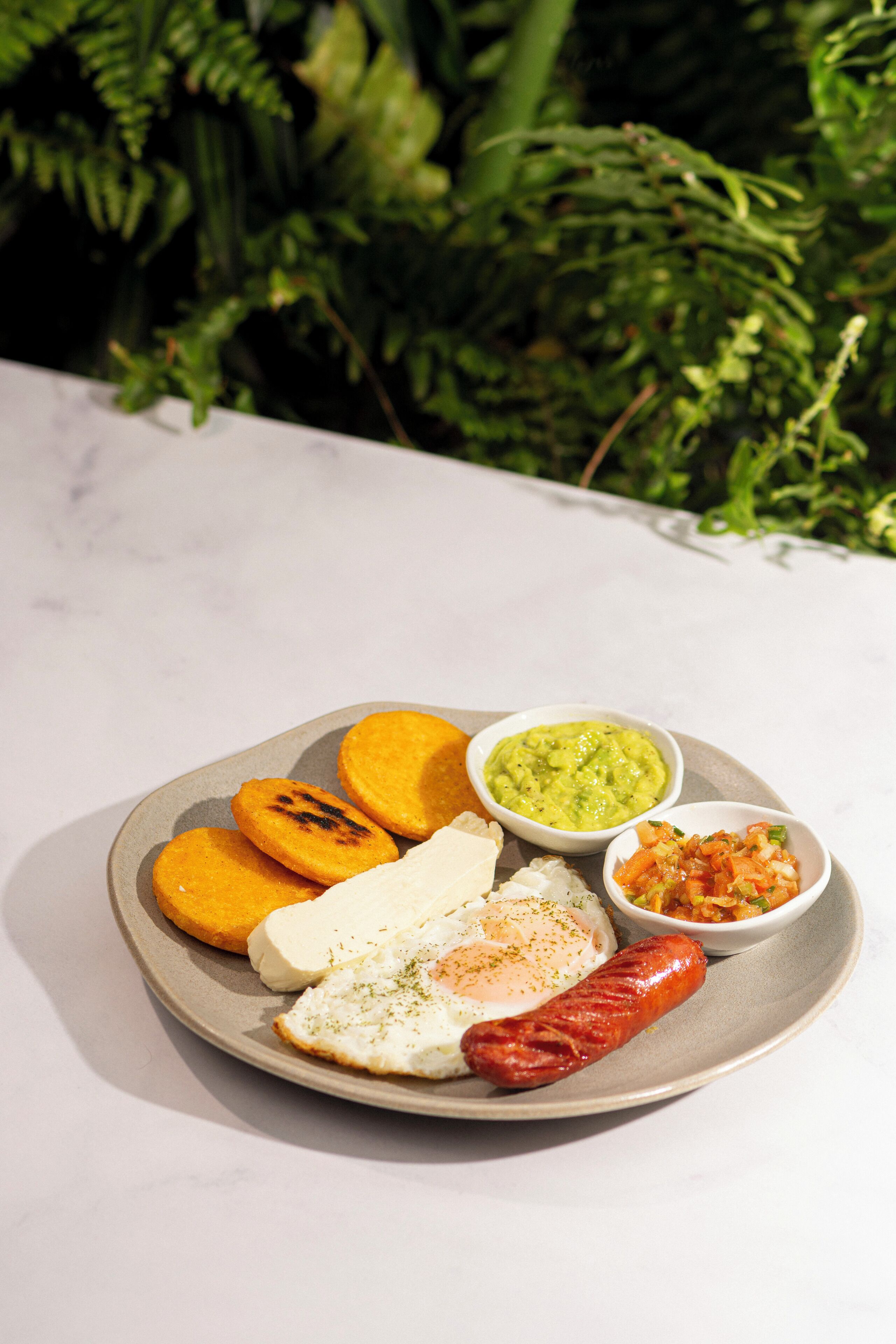 A plate with food items including a sausage, an egg, and a slice of cheese, accompanied by two small bowls of condiments.