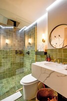 Un baño moderno con ducha de vidrio, inodoro blanco, lavabo de mármol y espejo con toallero.