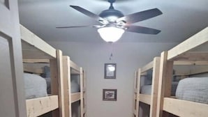 Ein schmales Gang mit Etagenbetten an beiden Seiten, einem Deckenventilator und einem gerahmten Bild an der Wand.