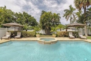 Ein Swimmingpool mit Liegestühlen und Sonnenschirmen, umgeben von Palmen und Grünpflanzen.