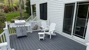Um deck com churrasqueira, cadeiras Adirondack brancas e uma mesa pequena.