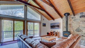 A cozy living room with a stone wall, a fireplace, and a large window overlooking a deck. - Ski Chalet|Ping-Pong|Fire Pit|5 min -> Slopes 🎿❄️🏂🌲🗻 (Bartlett)