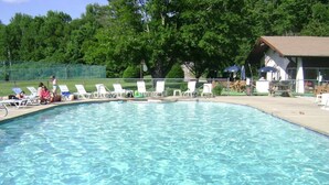 A swimming pool with clear water, surrounded by lounge chairs and a building with an American flag. - Ski Chalet|Ping-Pong|Fire Pit|5 min -> Slopes 🎿❄️🏂🌲🗻 (Bartlett)