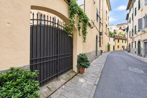 A narrow street with a closed gate, a potted plant, and a building with a tiled roof. - Casa Clara Luxury with Terrace (Lucca)