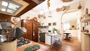 A kitchen with a stove, sink, and island with stools. There are hanging pots and a wooden cabinet. - Casa Clara Luxury with Terrace (Lucca)