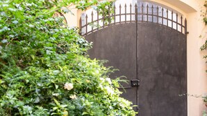 A large, dark metal gate with a decorative top, set within a lush green garden area. - Casa Clara Luxury with Terrace (Lucca)