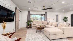 A modern living room with a sectional sofa, a coffee table, and a TV mounted on the wall. - The Rody - Mins to Old Town with Heated Pool, Games, Fast Wifi and More... (Scottsdale)