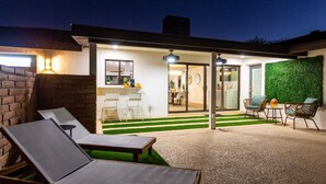 A modern outdoor patio with lounge chairs, a small table, and a green wall. - The Rody - Mins to Old Town with Heated Pool, Games, Fast Wifi and More... (Scottsdale)