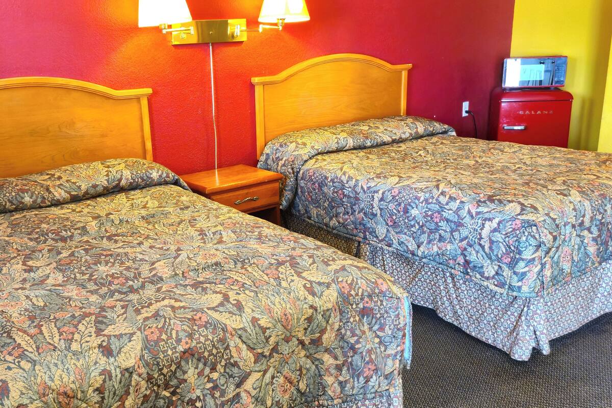 Une chambre d’hôtel avec deux lits, une table de chevet, une lampe et un appareil électroménager rouge.