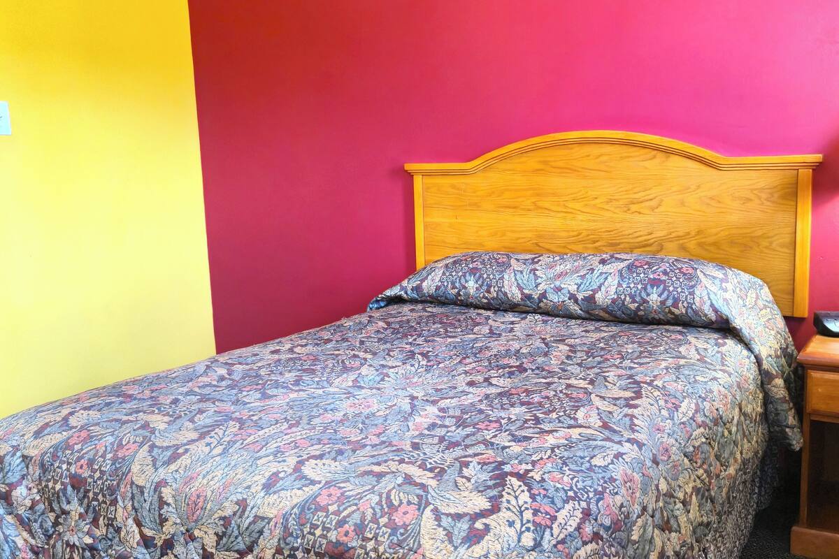 Un lit avec une couvre-lit à motifs floraux et une tête de lit en bois, le tout placé devant un mur rouge.