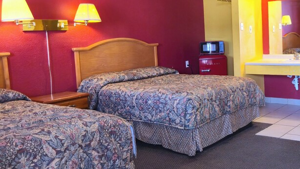 A hotel room with two beds, a wooden headboard, a red nightstand, a television, and a bathroom with a yellow sink and mirror. - Relax Inn By OYO Sulphur Hwy 90 (Sulphur)