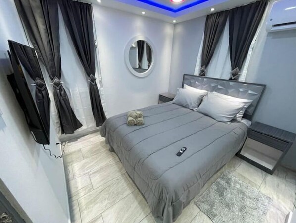 A modern bedroom with a grey bed, a round mirror, and black curtains.