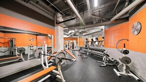 Une salle de sport équipée de divers appareils d’exercice, de miroirs et dont les murs sont peints en orange.