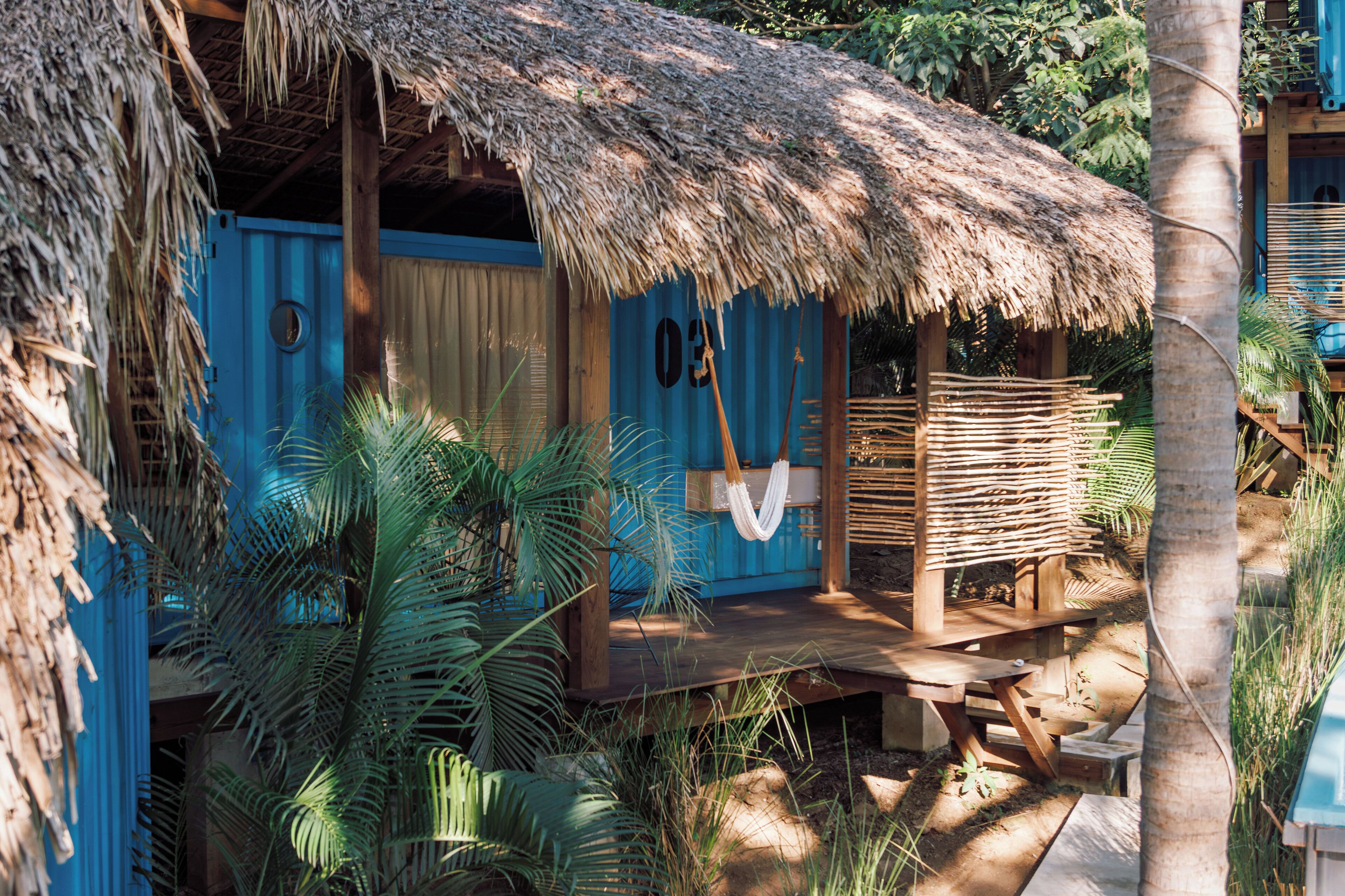 A thatched-roof hut with a wooden deck and a hanging hammock.