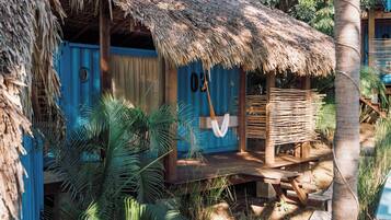 A thatched-roof hut with a wooden deck and a hanging hammock.