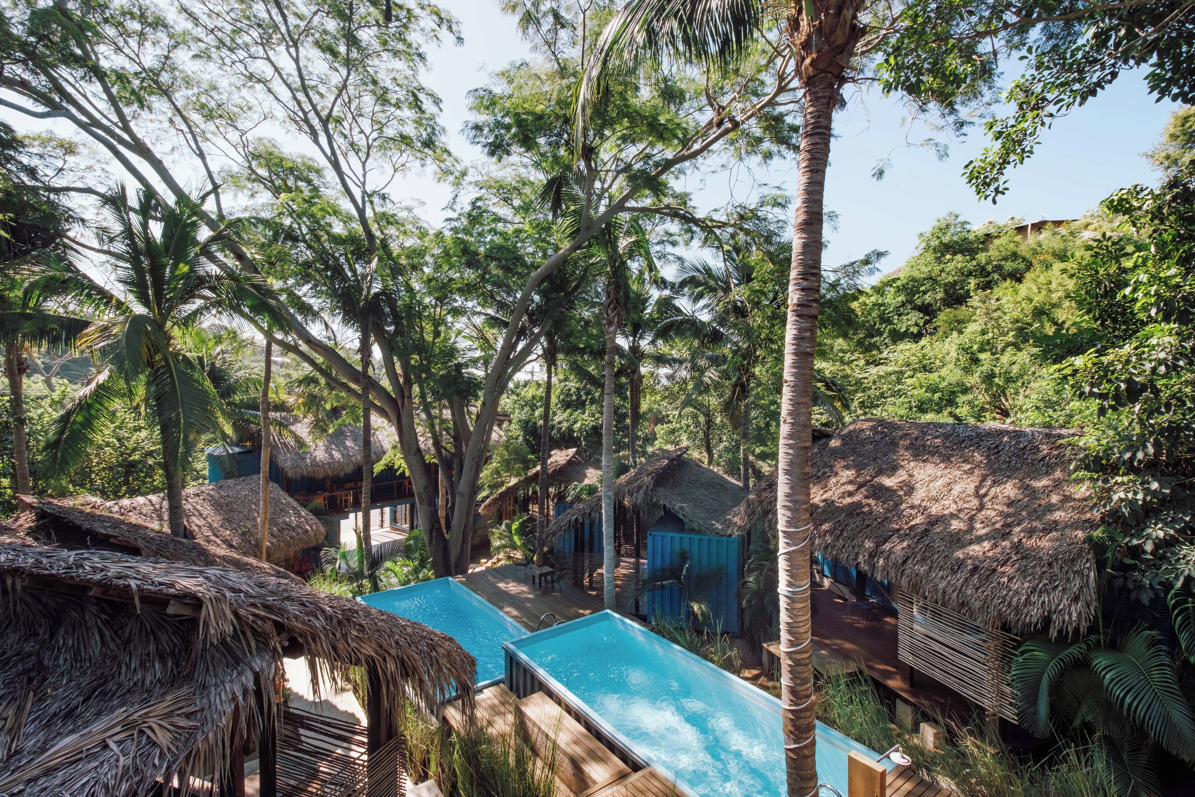 Una piscina rodeada de chozas con techo de paja en un entorno tropical exuberante.