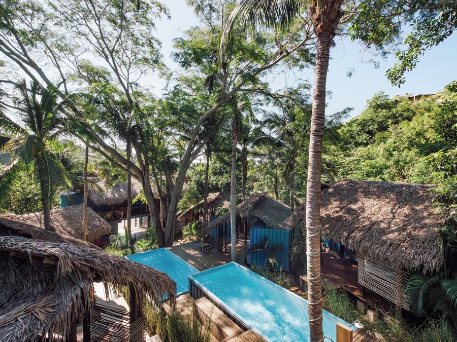 A pool surrounded by thatched-roof huts in a lush, tropical setting.