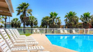 Zona de piscina con sillones blancos y palmeras.