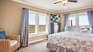 A bedroom with a bed, a dresser, a chair, and a view of the outdoors through large windows.