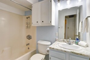 A bathroom with a bathtub, toilet, sink, and a mirror with lights. - Pompano- 2 Min Drive to Beach! | Sleeps 4 (Port Aransas)