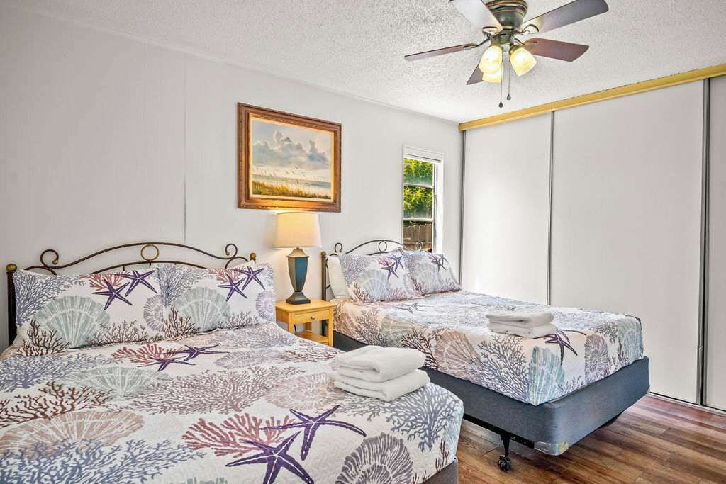 A bedroom with two beds, a ceiling fan, a bedside table with a lamp, and a framed picture on the wall.