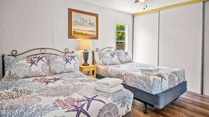 Une chambre avec deux lits, un ventilateur de plafond, une table de chevet avec une lampe et un tableau encadré au mur.