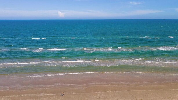 Une plage avec une eau d’un bleu limpide et un rivage sablonneux.