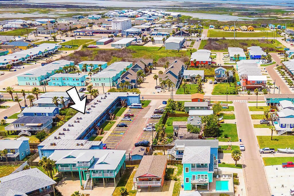 An aerial view of a coastal town with multiple buildings, including a large hotel with a swimming pool and a parking lot.