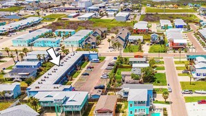 Vue aérienne d’une ville côtière avec de nombreux bâtiments, dont un grand hôtel doté d’une piscine et d’un parking.