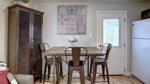 A dining area with a wooden table and four chairs, a cabinet, a potted plant, and a decorative tile wall. - Kona Cottage~Dog Friendly~In Town Location (Port Aransas)