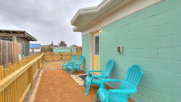 A building with turquoise walls and a wooden deck. There are turquoise chairs arranged on the deck. - Kona Cottage~Dog Friendly~In Town Location (Port Aransas)