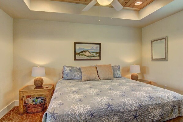 A bedroom with a bed, two nightstands, a ceiling fan, a framed picture on the wall, and a wicker basket on one nightstand.