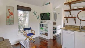 A room with a wooden desk, a chair, a television, and a kitchen area with a dishwasher.