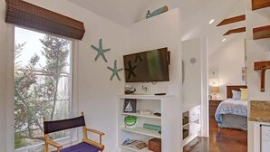 A room with a large window, a television, a bookshelf, and a bed.