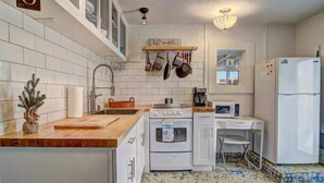 A compact kitchen with white cabinets, a wooden countertop, a stove, a microwave, and a refrigerator.