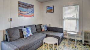 A living room with a grey sofa, a small white table, and a window with blinds.