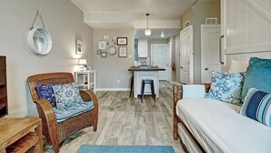 Un dormitorio acogedor con una cama, una silla, una mesita y una kitchenette al fondo.