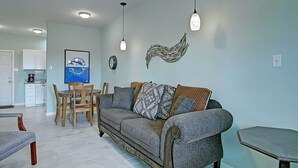 Ein Wohnzimmer mit einer Couch, einem Esstisch und Stühlen. Im Hintergrund ist eine Küchenzeile zu sehen.