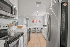Uma cozinha moderna com eletrodomésticos de aço inoxidável, uma mesa de jantar de madeira e piso claro.