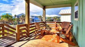 Um deck de madeira com cadeiras e uma mesa, com vista para uma área residencial com casas e palmeiras.