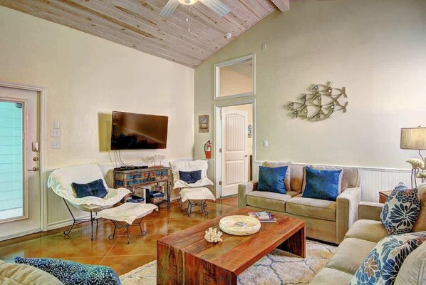 Un salon spacieux doté d’un plafond en bois, d’un grand téléviseur à écran plat, d’un ensemble de canapés et d’une table basse.