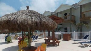 Une terrasse au bord de la plage, dotée de sièges extérieurs et d’un parasol en chaume.