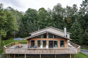 A two-story wooden cabin with a deck, large windows, and a chimney.