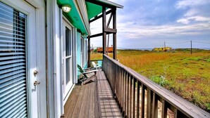 Een houten terras met een balustrade, een overdekte veranda en uitzicht op een grasveld.