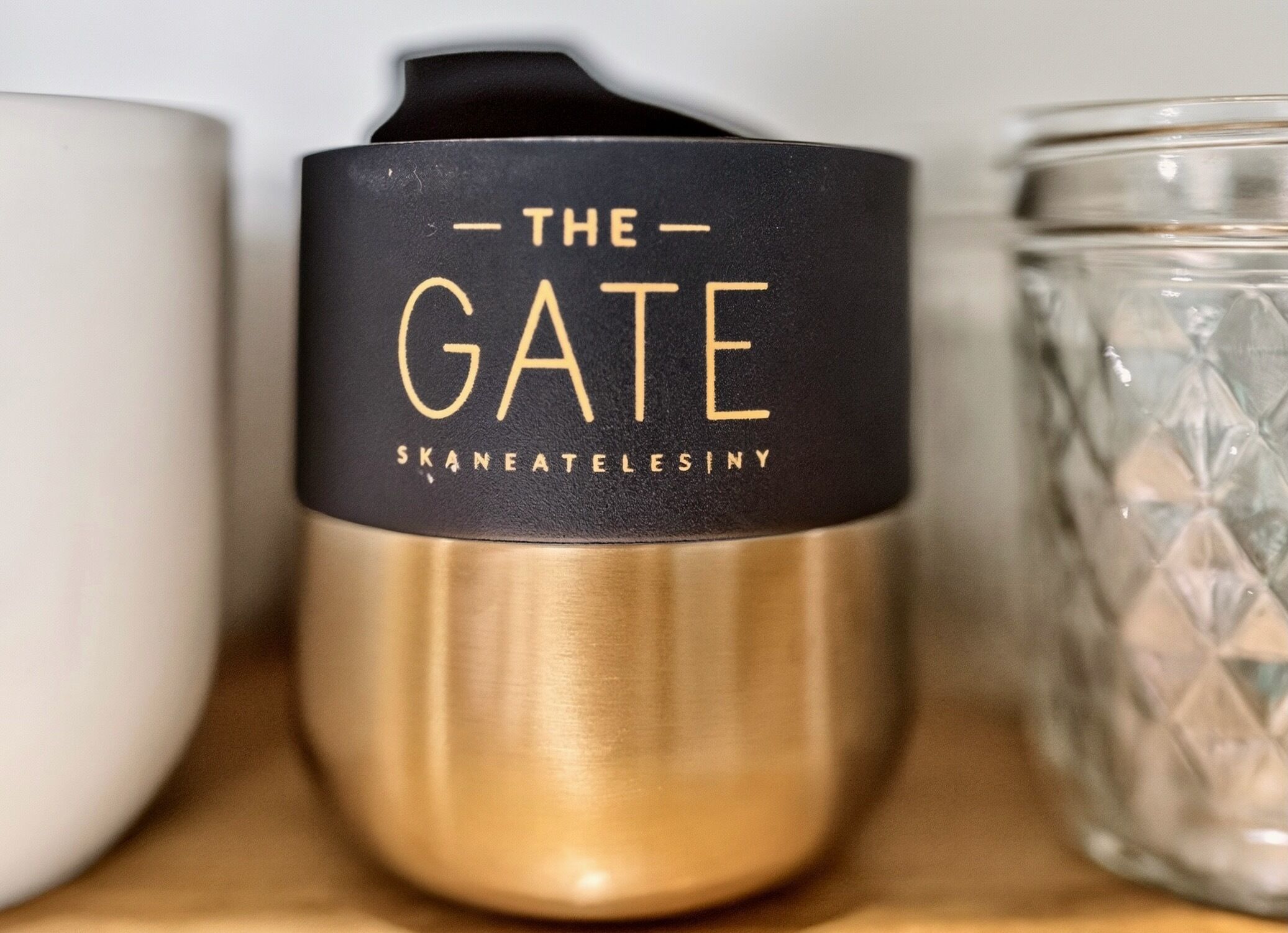 Una vela con tapa negra y detalles dorados, etiquetada 'THE GATE SKANEATLESINY'.