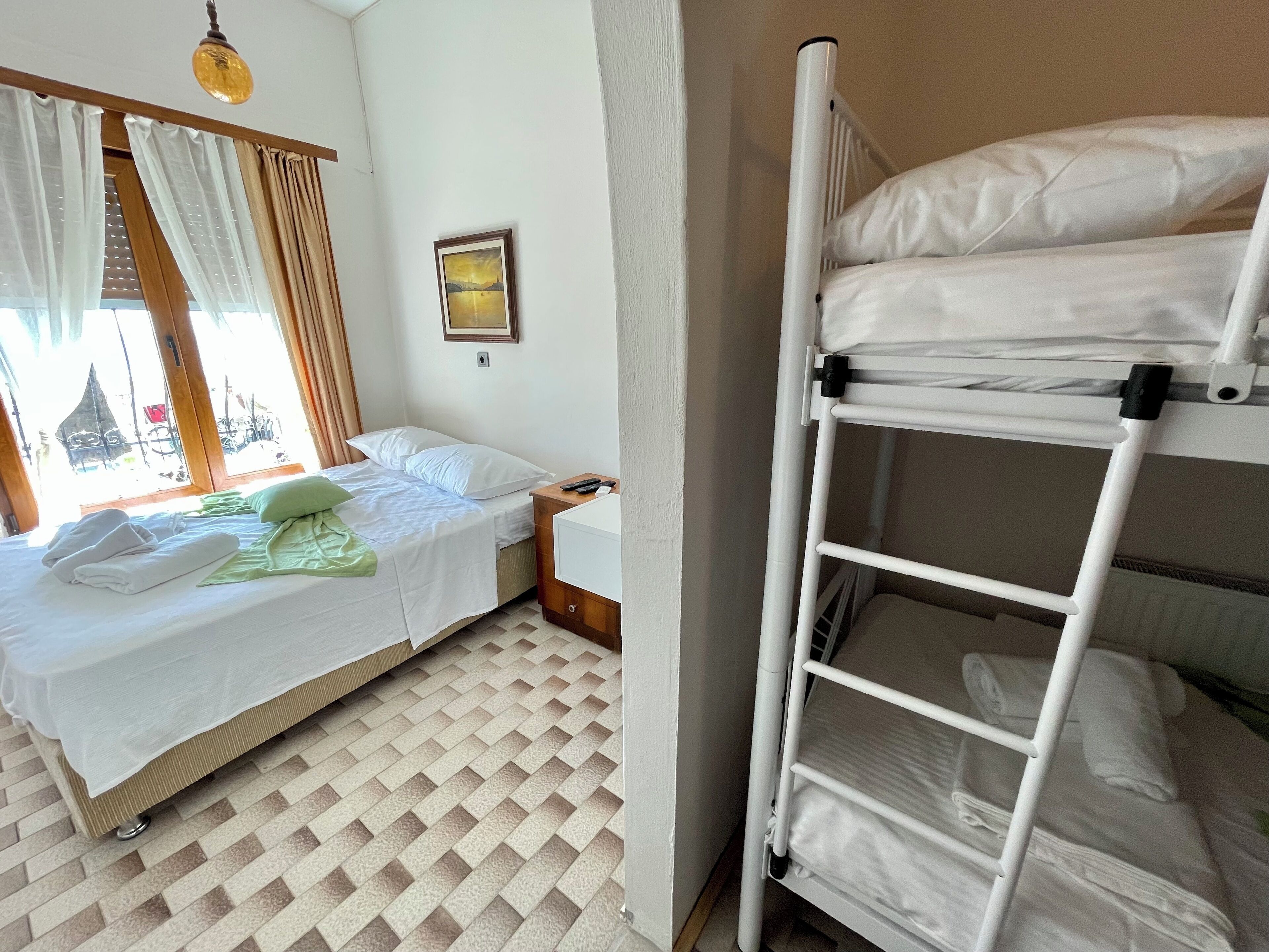 Habitació amb un llit, un llit superposat, una finestra amb cortines, un quadre a la paret i un radiador.