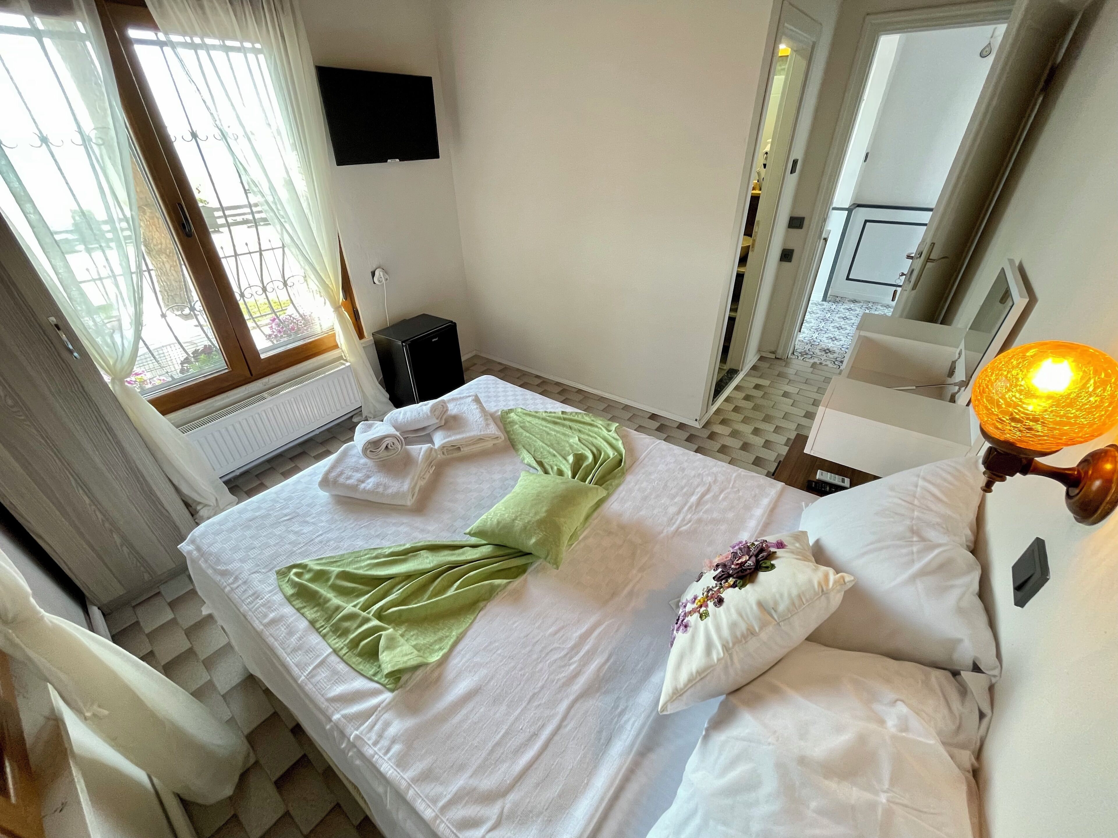 Een hotelkamer met een bed, een flatscreen televisie aan de muur, een radiator en een raam met gordijnen.